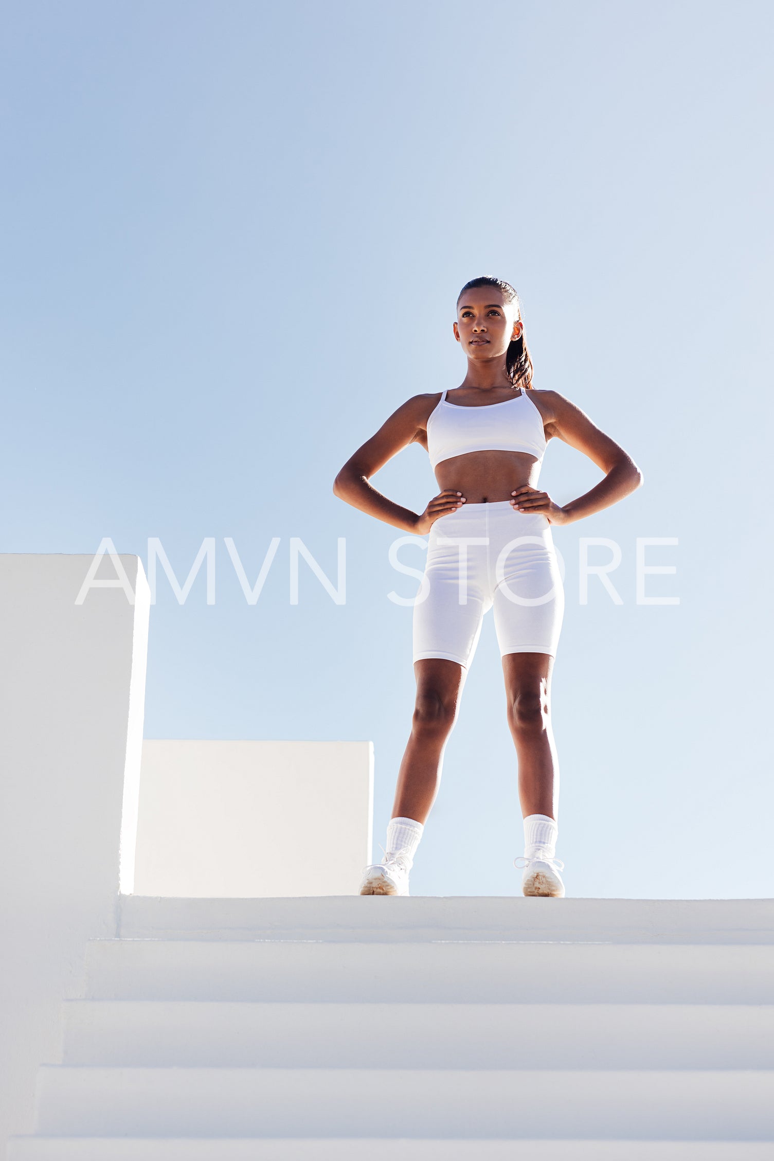 Full length of young slim sportswoman relaxing. Woman with hands on hips standing on the top of stairs.