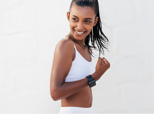 Cheerful woman flexing her hand showing muscles. Smiling female in white fitness attire strains the biceps.