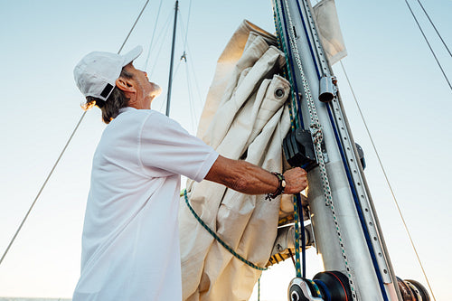 Mature captain looking up while adjusting sail. Senior yachtsman preparing a boat for a vacation trip.