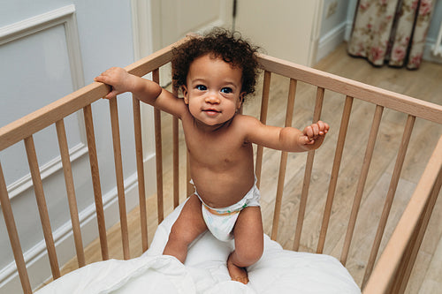 Toddler boy standing in a crib. Smiling child trying to walk.