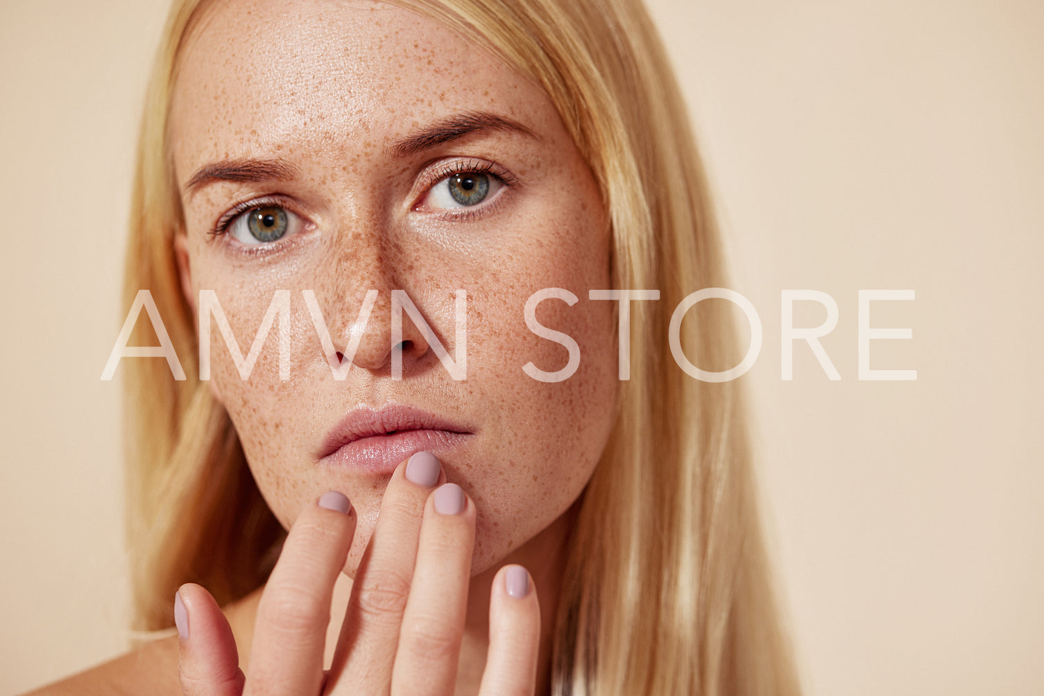 Close up of a woman with freckles touching her lip with a finger. Young blond female applying balm on her lips.