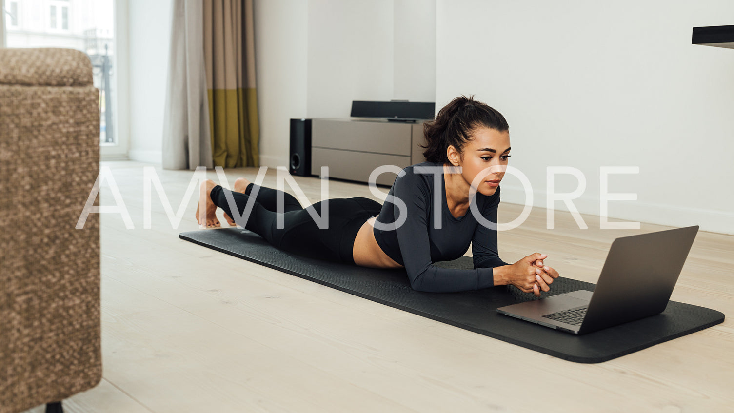 Woman in sport clothes lying on mat in living room watching fitness instructor online	