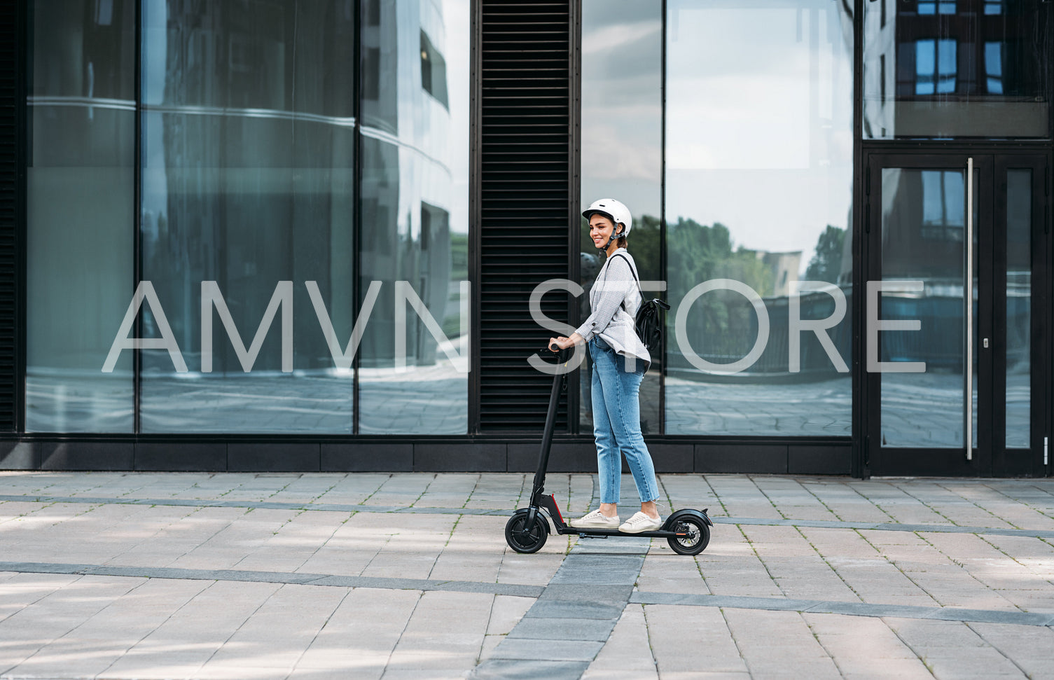 Young businesswoman wearing cycling helmet riding push scooter on footpath