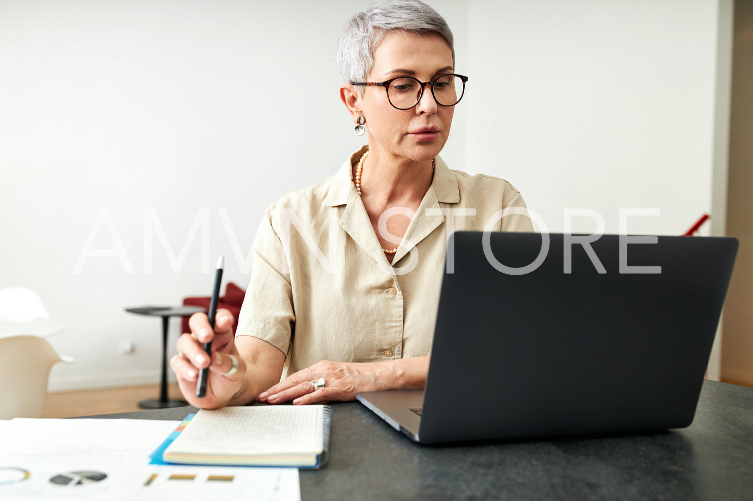 Mature woman looking on laptop screen holding a pen