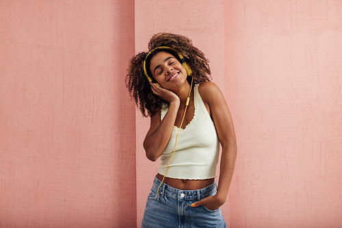 Woman with curly hair relaxing at pink wall listening to music w