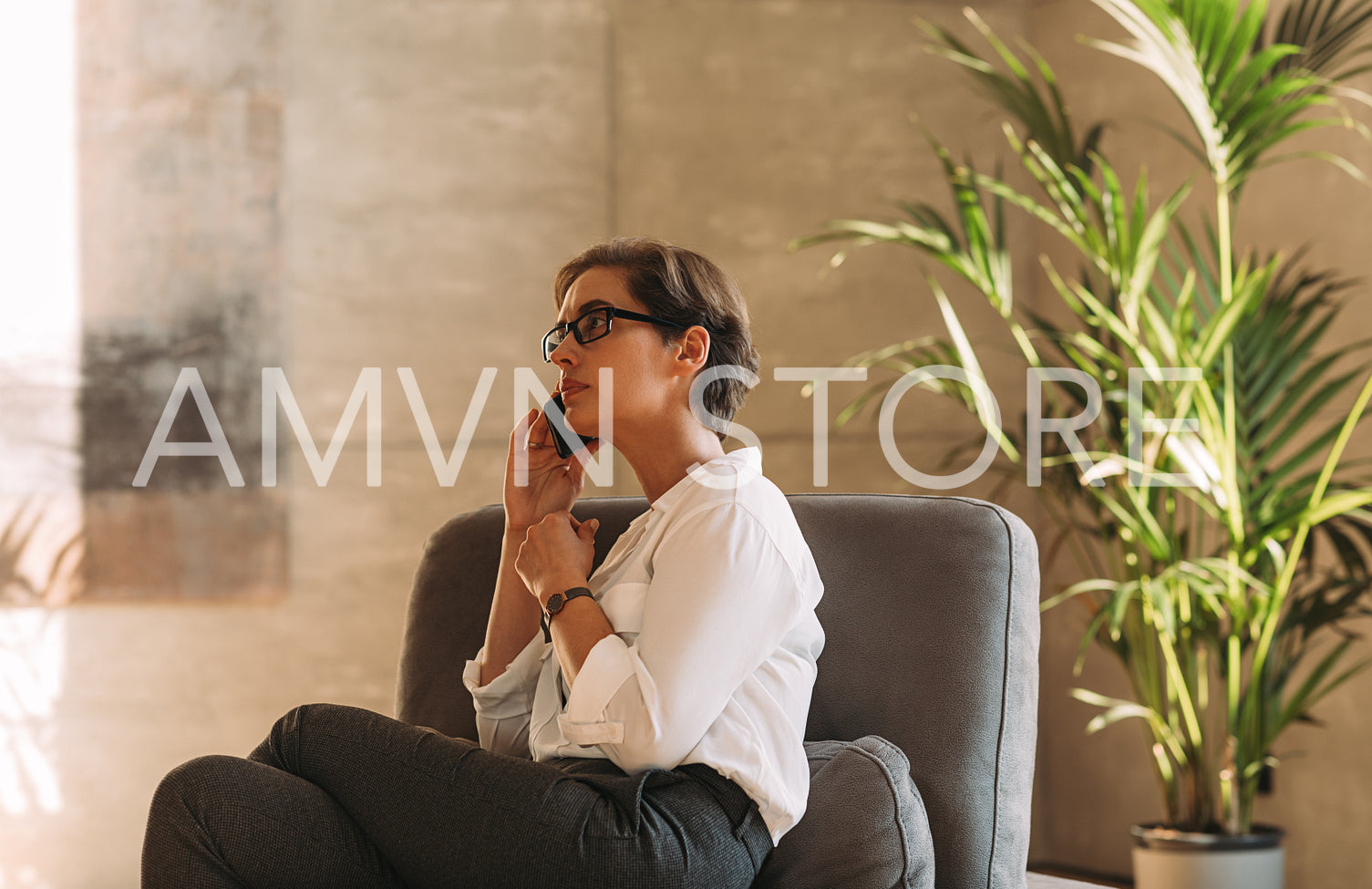 Side view of a middle-aged woman in formal wear sitting indoors and talking on a mobile phone