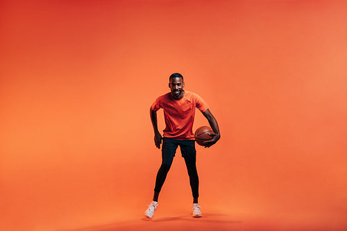 Young sportsman dribbling basket ball in studio against an orange background
