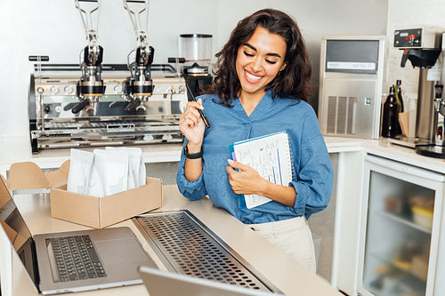 Smiling entrepreneur woman standing at a table in coffee shop. Happy businesswoman in her cafe.