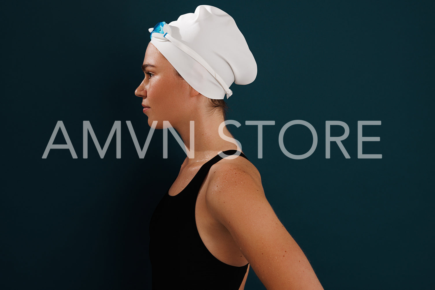 Side view of a woman swimmer standing at blue wall, wearing swimming cap and glasses