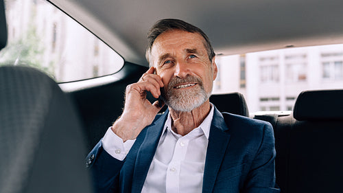 Smiling senior man talking on cell phone while sitting in taxi looking away