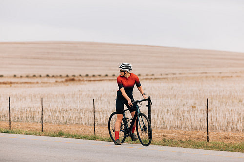 Woman cyclist standing on road with bike and looking back preparing to move