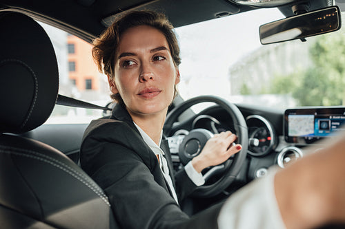 Portrait of caucasian businesswoman driving a car in reverse looking on back window