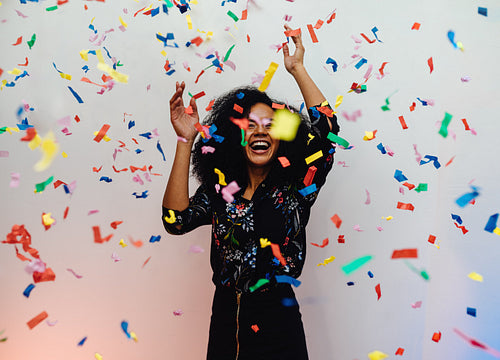 Young woman dancing under confetti at home, celebrating birthday