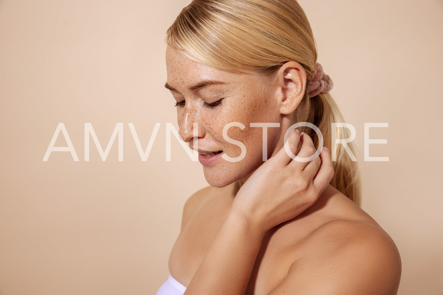 Portrait of a woman with freckles touching her neck in studio