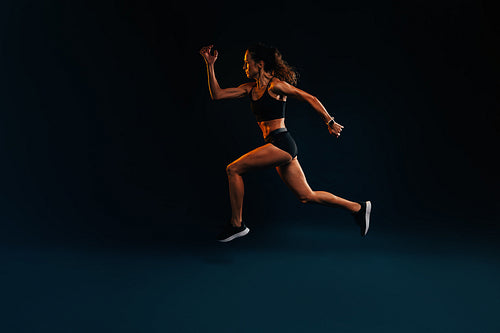 Sprinter against a black background. Muscular female running and jumping.