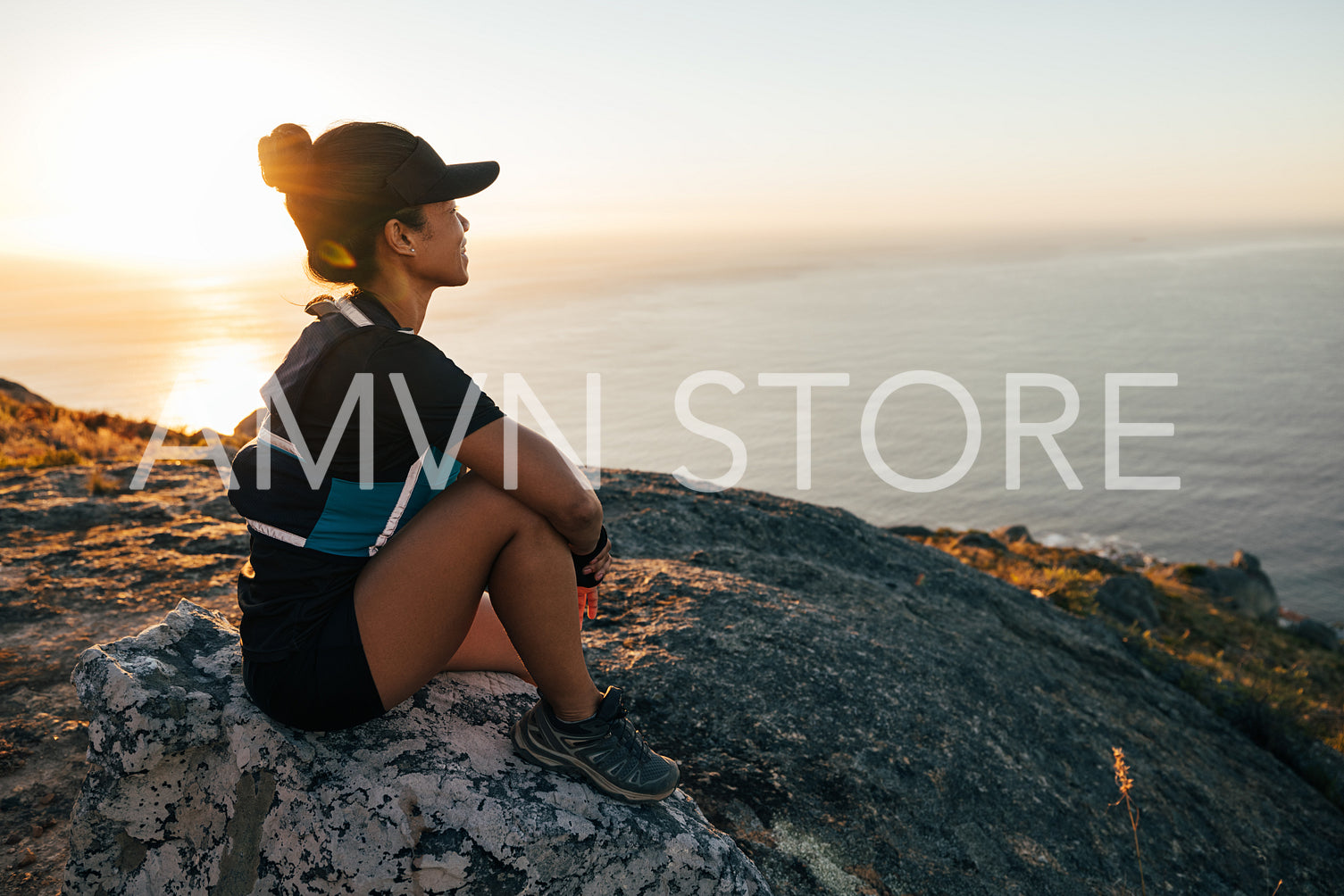 Woman in sportswear enjoying the sunset. Female hiker sitting on rock and looking into a distance.