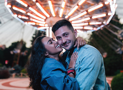 Young couple embracing and having fun in amusement park against carousel