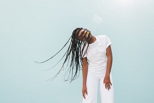 Young happy woman in white casuals standing outdoors while her face covered by long braids