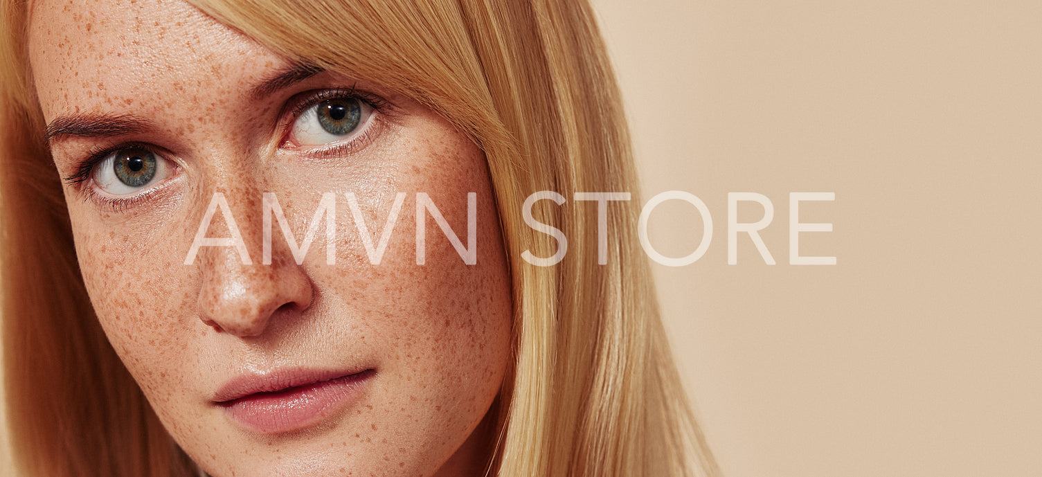 Close-up studio shot of a young beautiful female with naturally smooth skin. Cropped studio shot of woman with freckles looking at camera over beige backdrop.