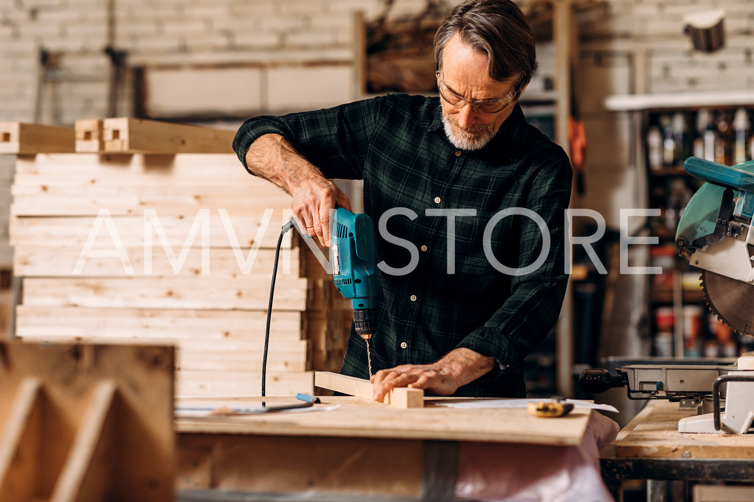 Carpenter using electric drill. Senior man making a hole in a wooden board.	