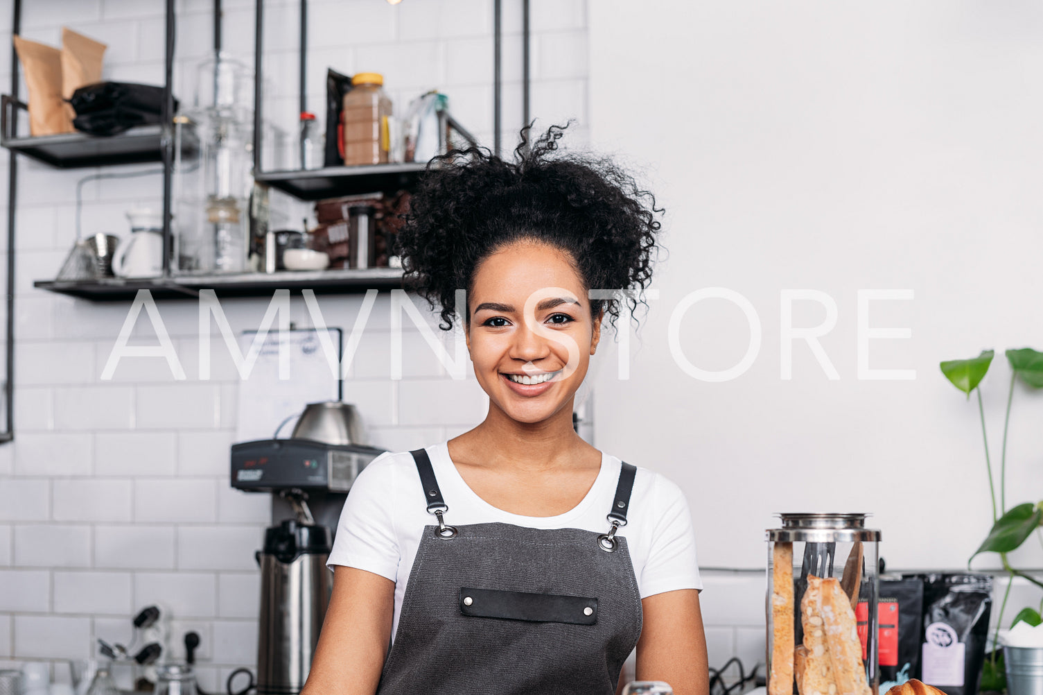 Portrait of a young smiling female barista with curly hair looking at camera