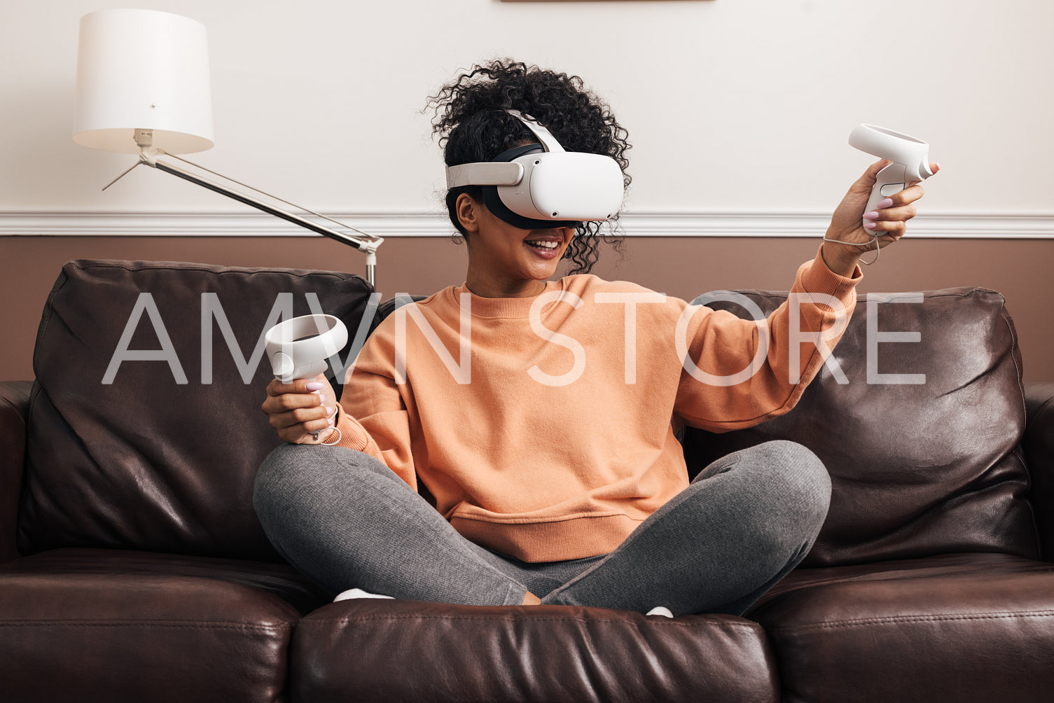 Woman with joysticks and VR goggles playing video games on a sofa