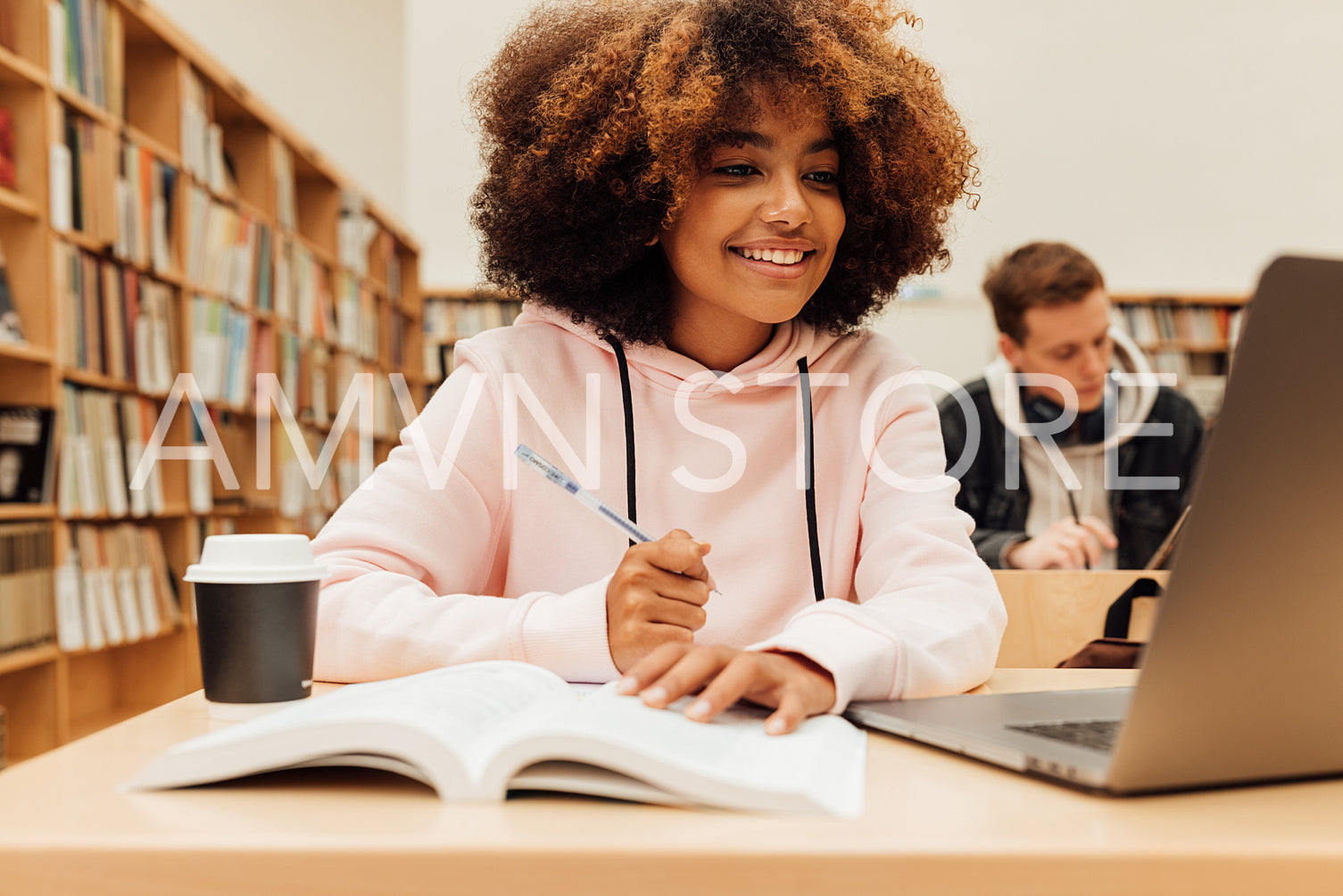 Smiling girl sitting at a table in the library and looking at a laptop