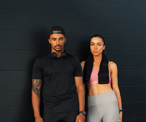 Multiethnic fit couple in sportswear relaxing at a black wall outdoors