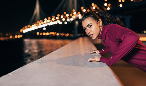 Young mixed race female athlete doing push-ups on an embankment at evening