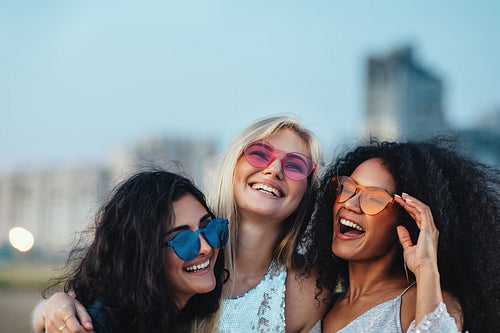 Three beautiful women with colorful sunglasses standing at evening outdoors