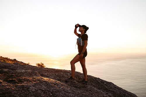 Side view of young woman looking up during hike. Trail runner going up on mountain at sunset.