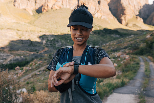 Smiling woman hiker in cap checking activity on smart watch during her hike