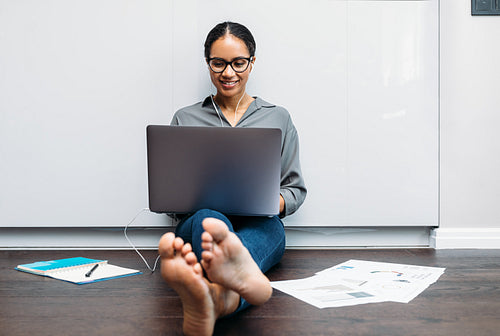 Smiling freelancer sitting on floor at home working on a laptop computer