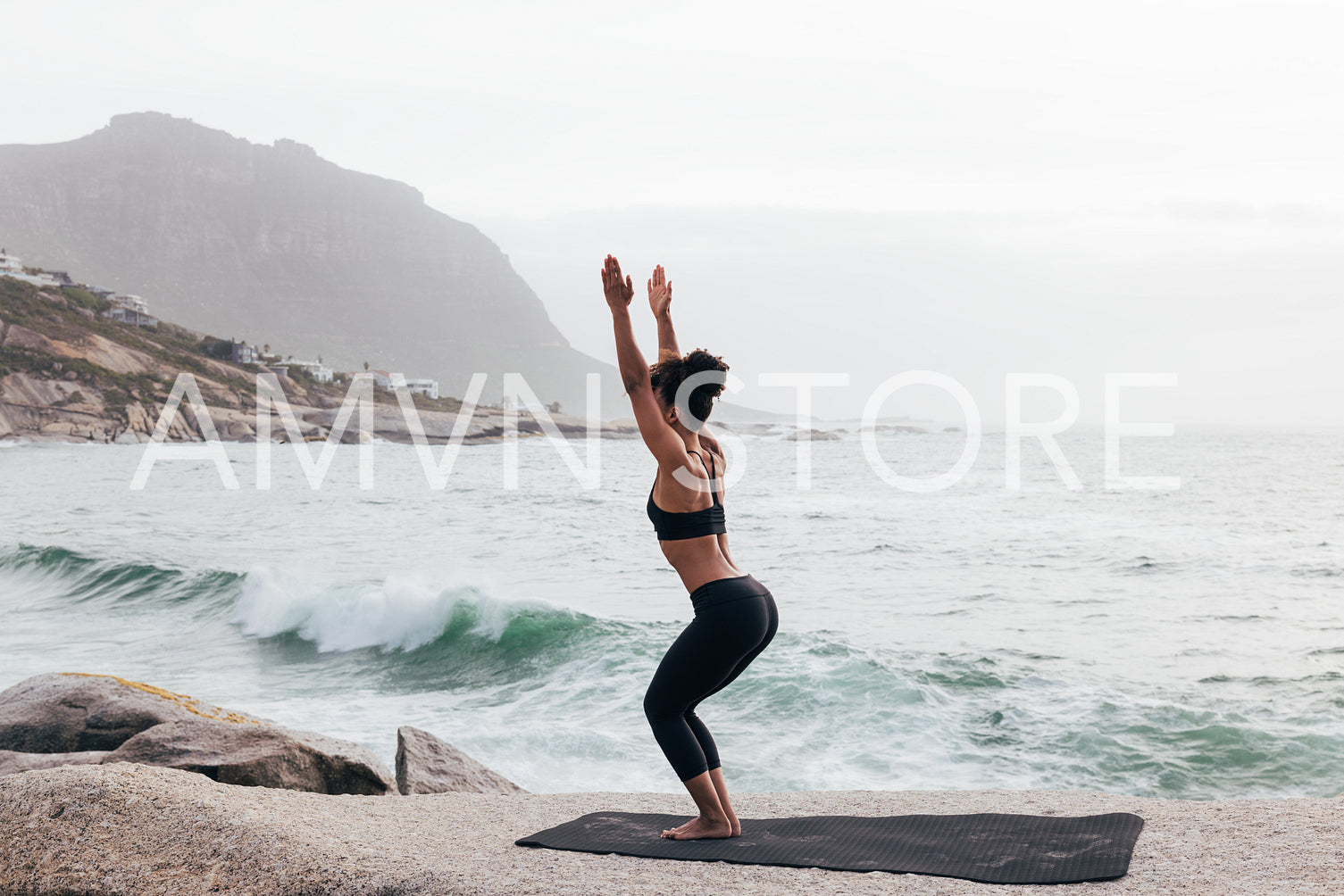 Young woman doing Utkatasana pose by ocean. Slim female in practicing Chair Pose at evening by seaside.