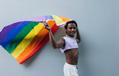 Smiling guy with rainbow flag at wall outdoors. Stylish man with lgbt flag.