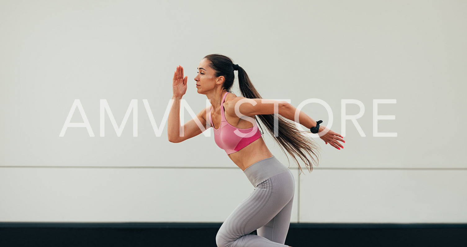 Side view of slim woman with long hair in sportswear running at a wall 