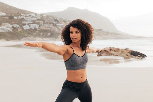 Female in sportswear practicing Warrior pose while standing on beach at sunset