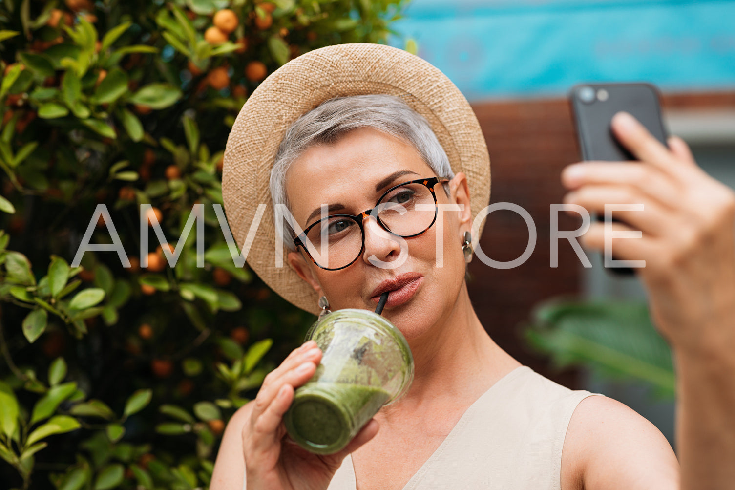 Aged stylish woman drinking a green smoothie and taking a selfie in the park