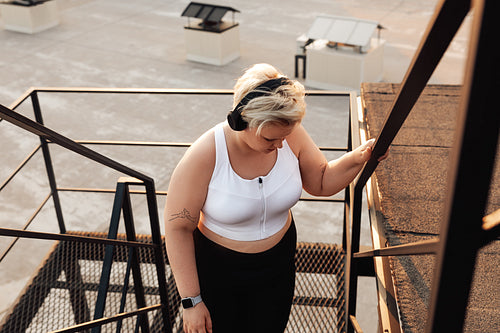 Plus size woman in sports clothes taking a break and looking down while standing on a staircase