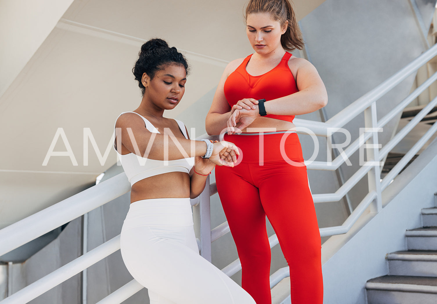 Two plus-size women in fitness attire are checking pulse during a workout. Young females in sports clothes are standing on stairs outdoors looking at smartwatches.