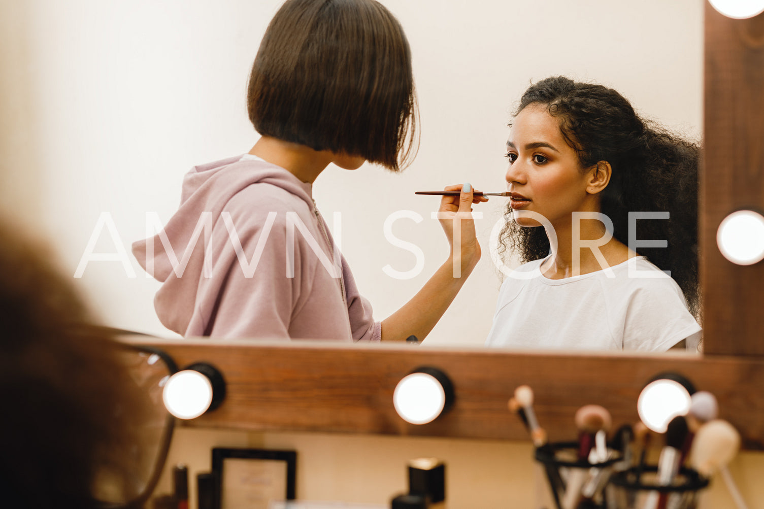 Professional make up artist applying pomade on a model in front of a mirror	