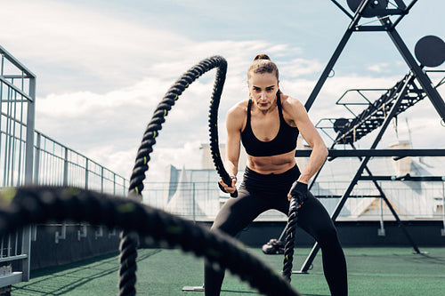 Woman in fitness wear working out with two battle ropes on rooftop