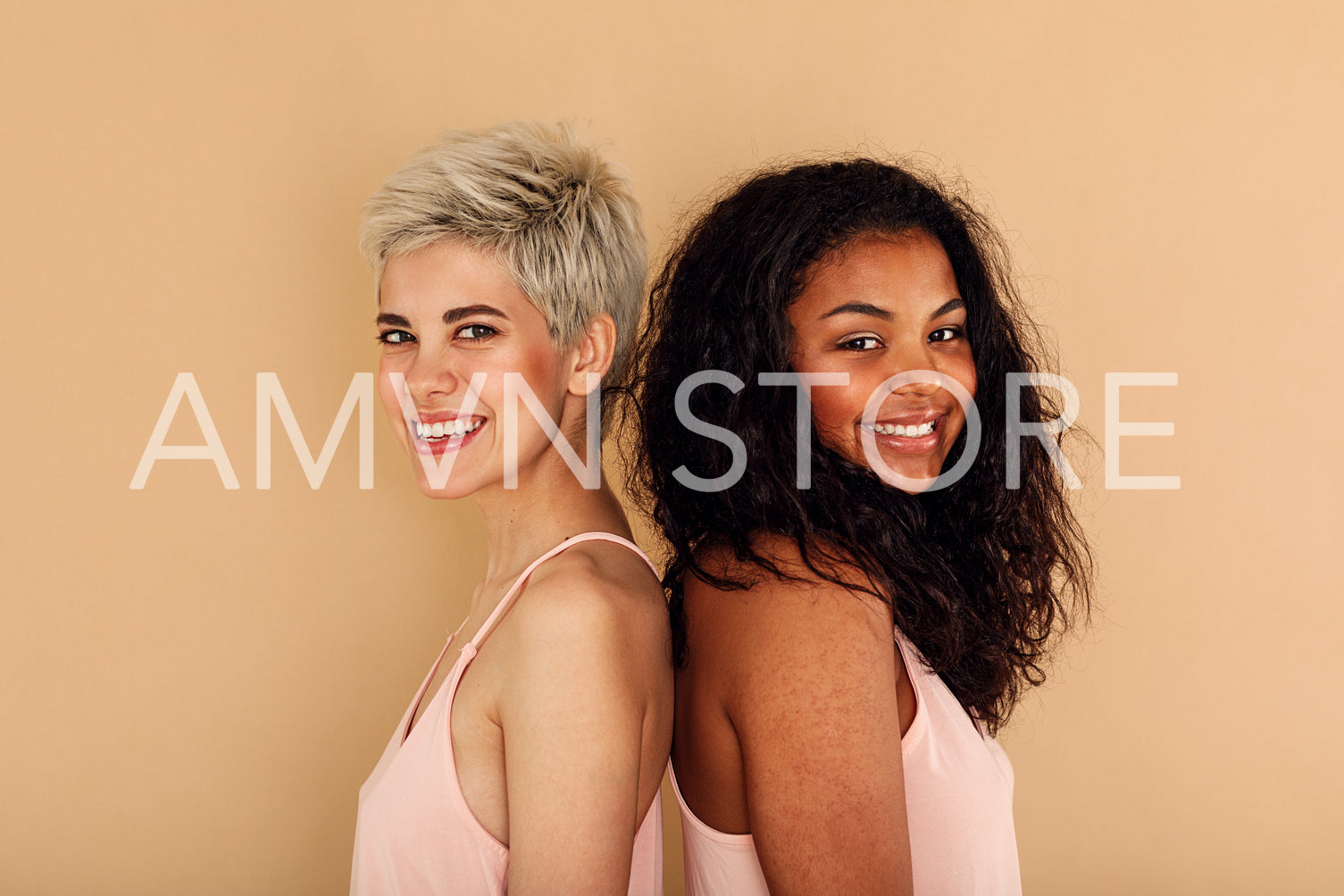 Two happy women posing back to back in studio	