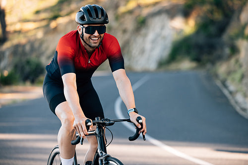 Young male cyclist smiling while riding a road bike on a hill