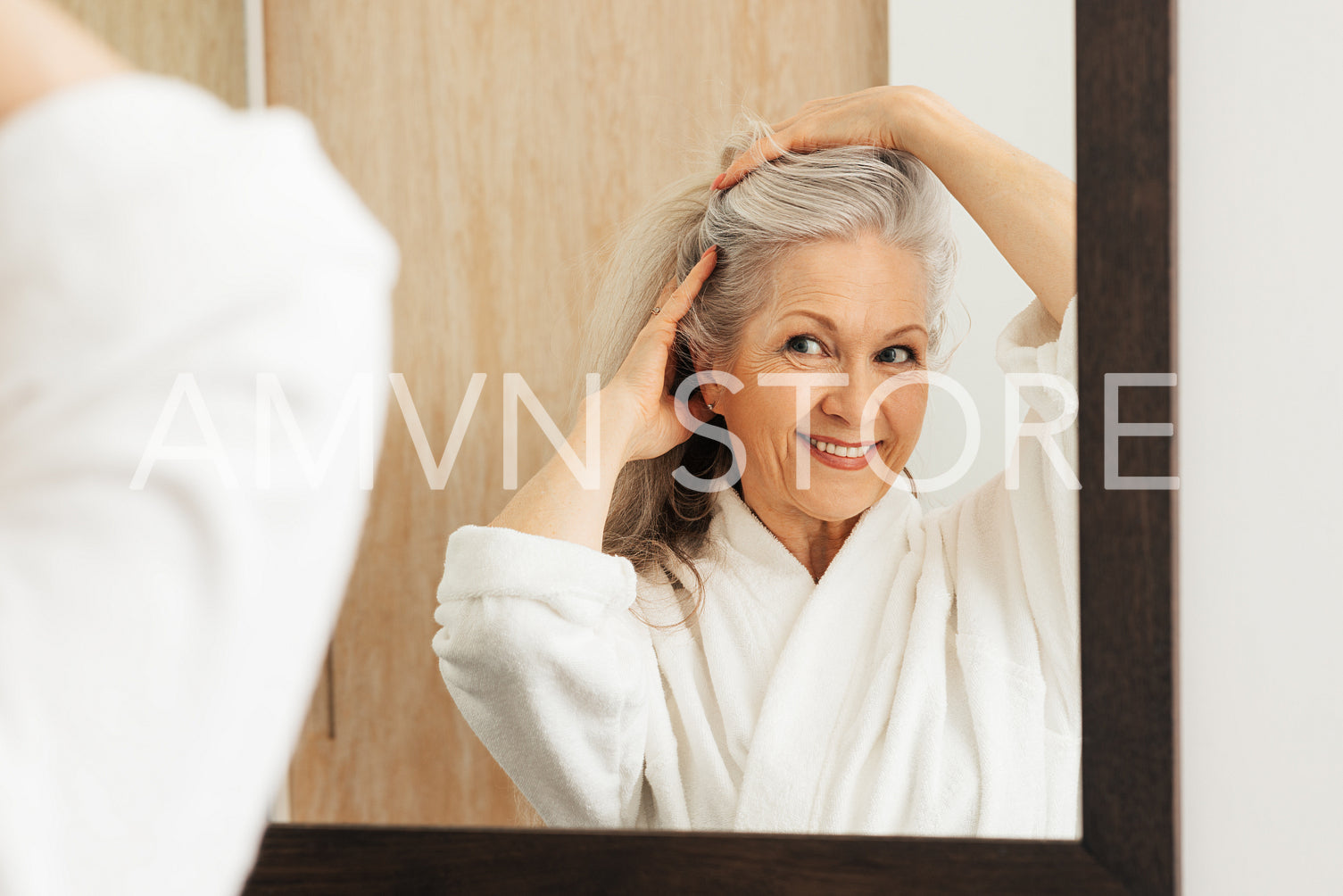 Smiling aged female making a new hairstyle by hands in front of a mirror