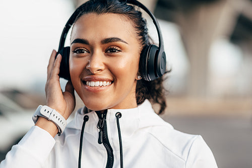 Female athlete with headphones resting after workout outdoors. Young fitness woman in sportswear listening to music.