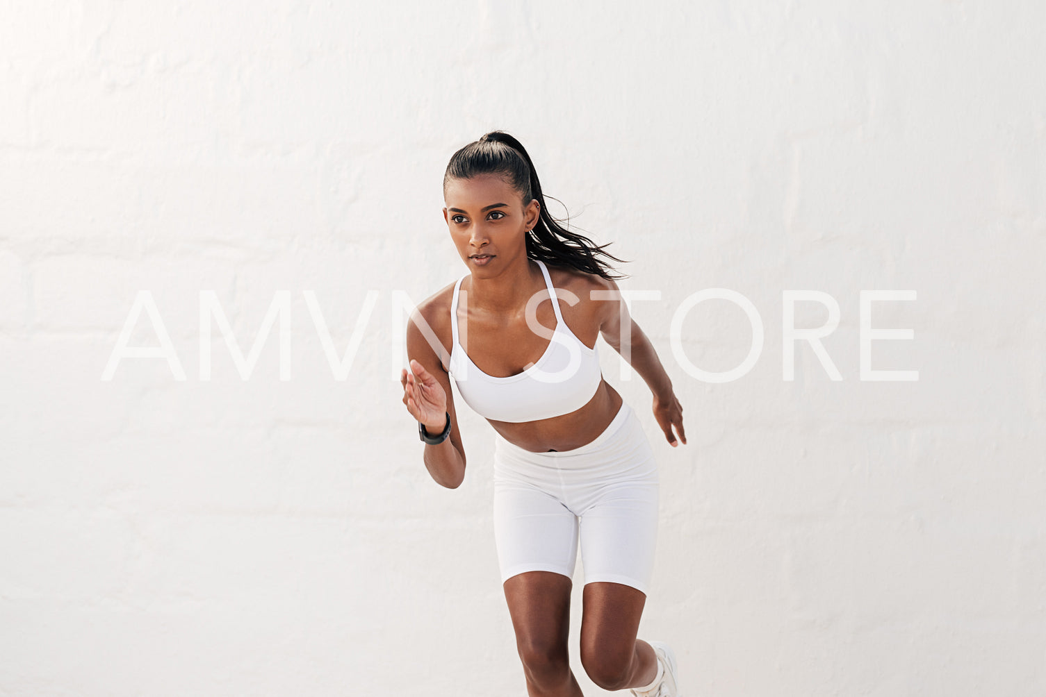 Young slim female athlete running outdoors against a white wall. Fitness influencer in white sportswear sprinting.