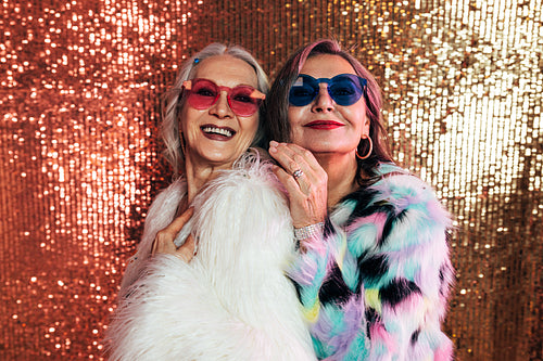 Two smiling senior women in fur coats posing together in studio