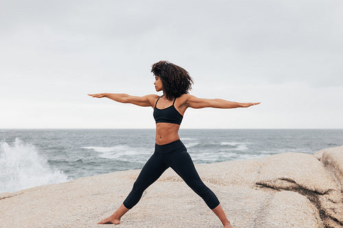 Side view of yong woman performing warrior pose against ocean