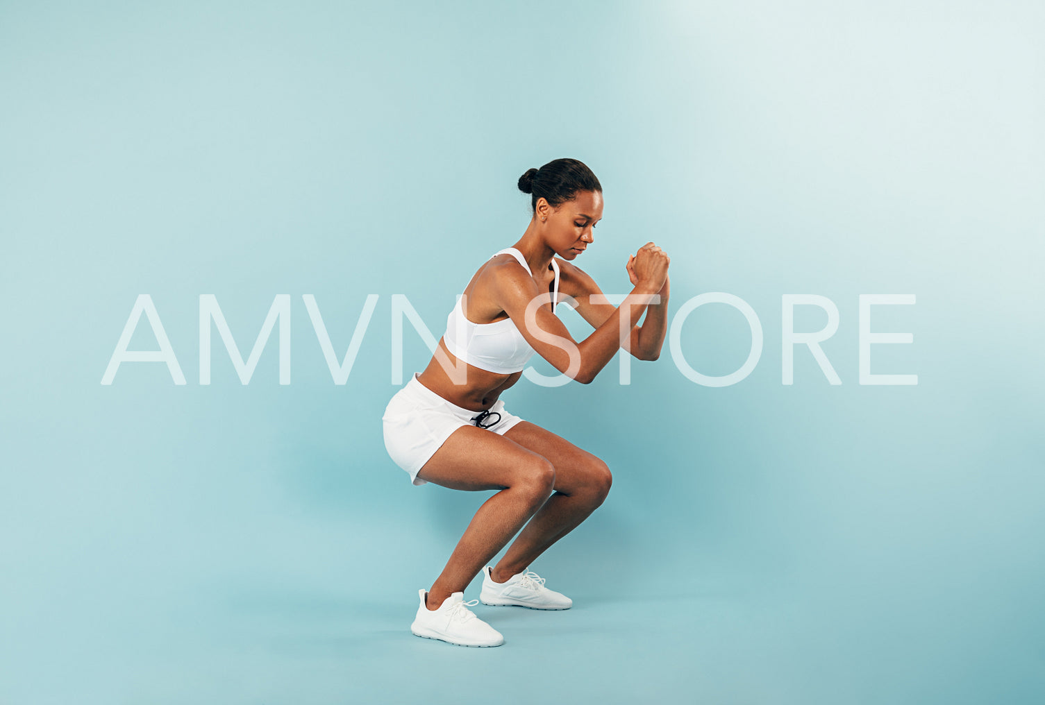 Side view of a young woman in sportswear doing squats at blue background in studio	